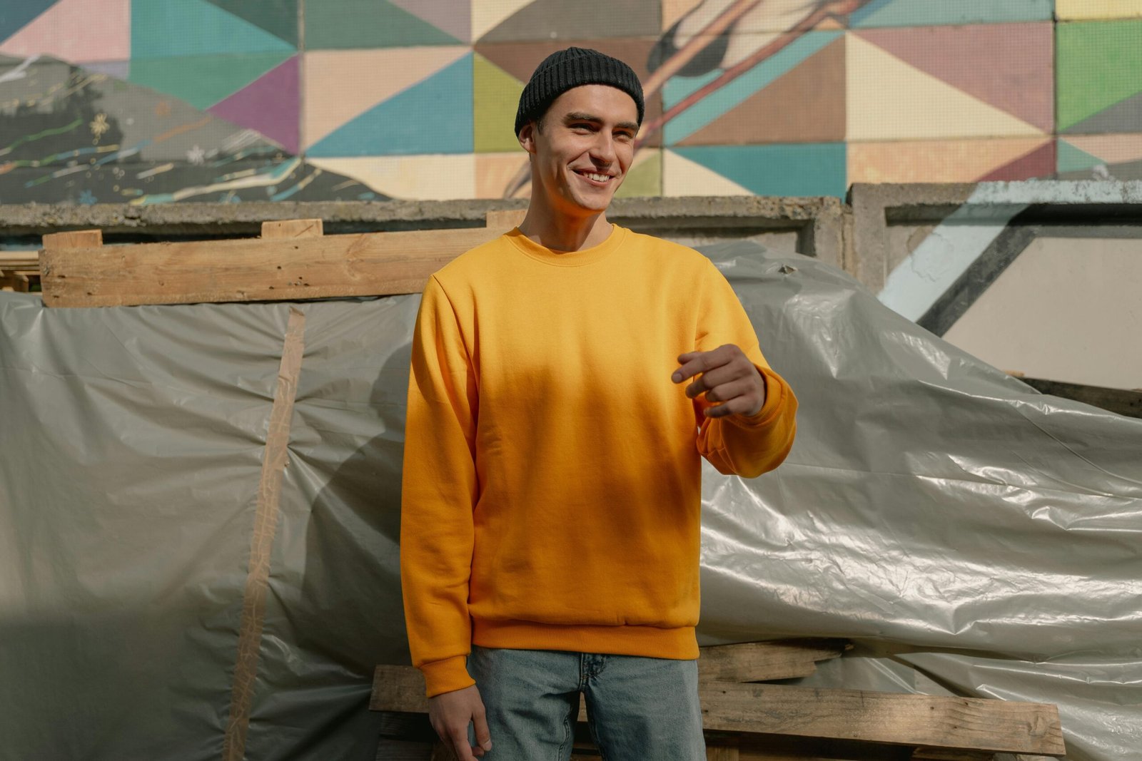 pexels-photo-5560217-5560217 A young man in a knit cap and yellow sweatshirt smiles in front of a colorful geometric wall.